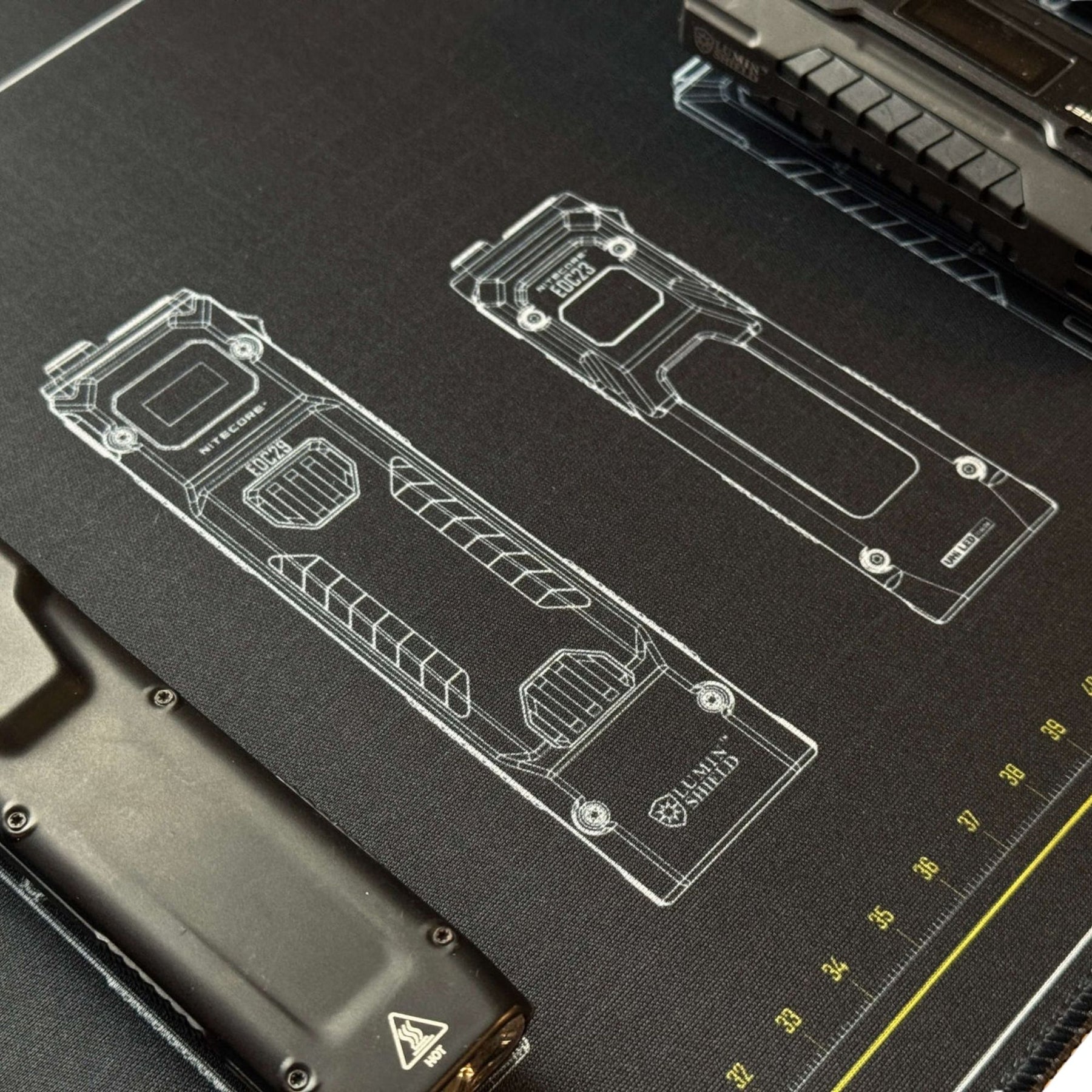 Nitecore Tappetino Mouse XL. Sottomano tecnico da scrivania con schemi grafici di torce serie EDC e righelli graduati sui bordi. Superficie ampia in tessuto morbido per manutenzione o gaming con loghi tecnologia Lumin Shield.