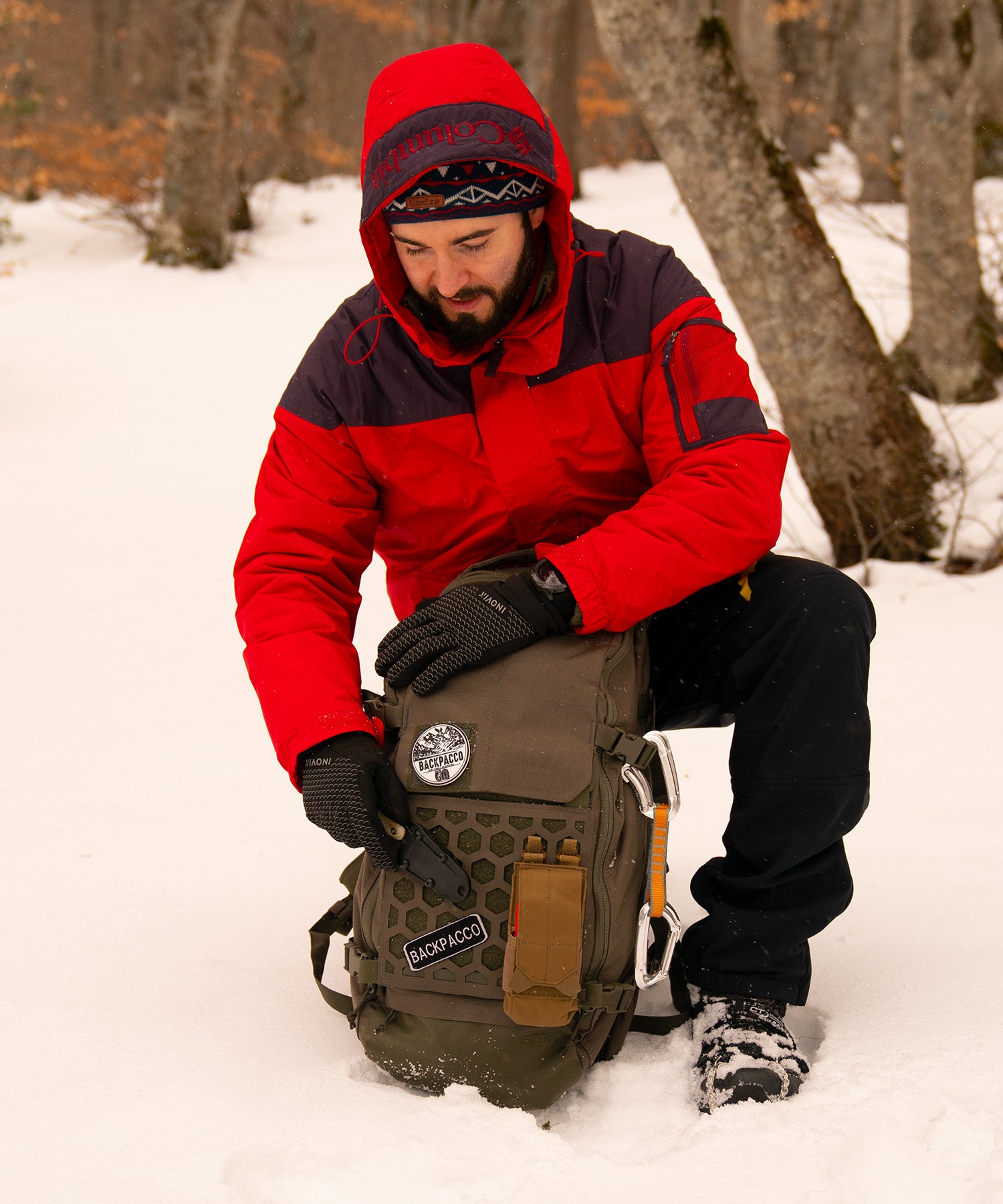 Paolo di backpacco estrae il coltello Izula 2 dallo zaino AMP24 Ranger Green durante un'escursione in montagna con la neve