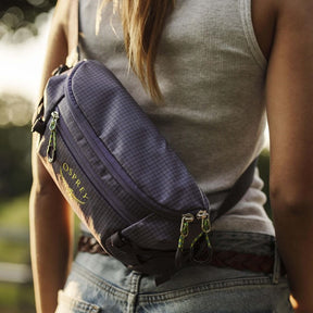 Osprey Transporter Waist Pack marsupio da 3 litri realizzato in tessuto tecnico con trama a griglia e logo frontale, dotato di tasca esterna con zip, cinghie di compressione laterali e cintura regolabile con fibbia a scatto per escursionismo e tempo libero.